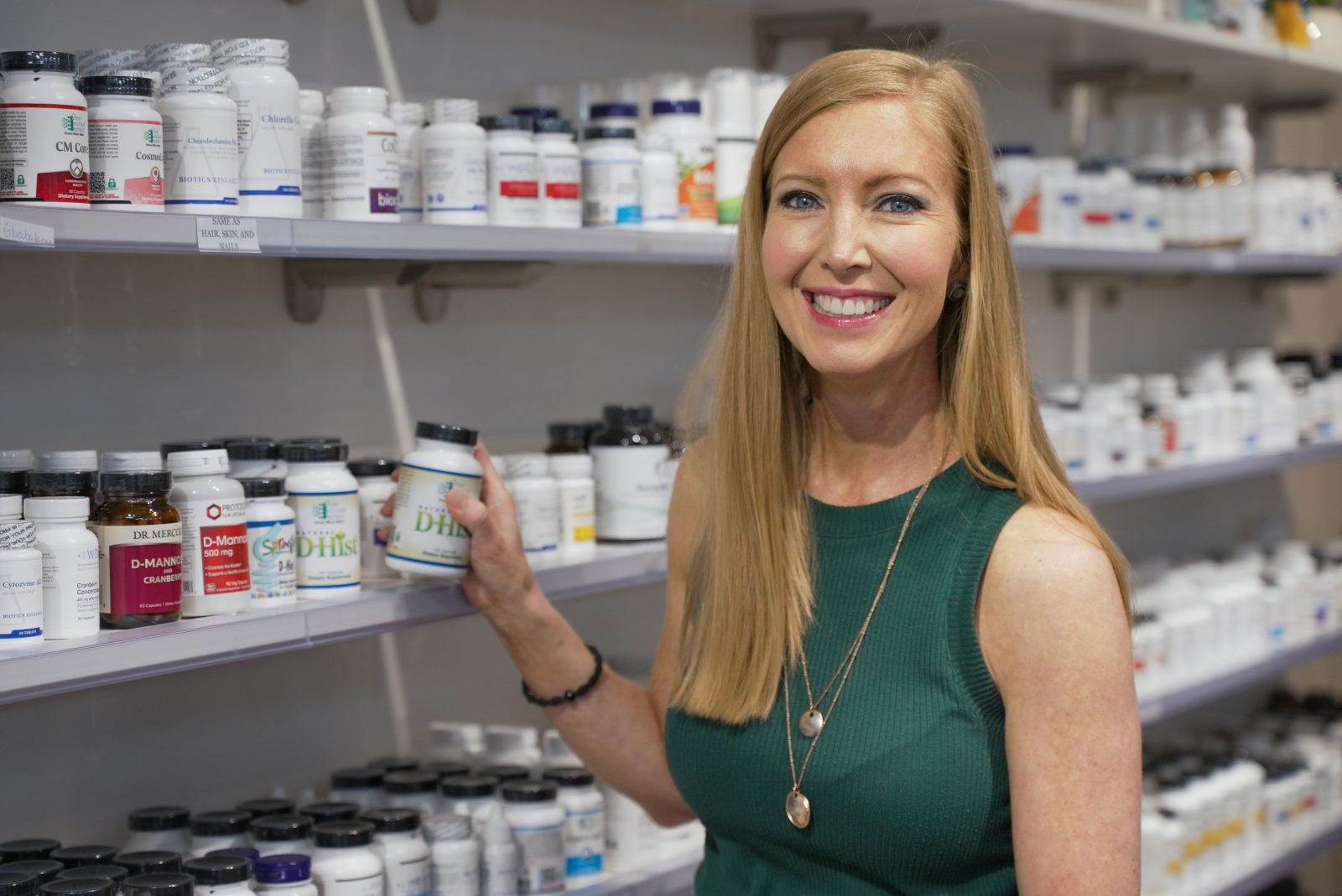 Jaime, a pharmacist at Williamsburg Drug Company, holding a professional-grade supplement in front of fully stocked shelves.